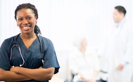 a nurse facing the camera while a doctor speaks to the patient in the background